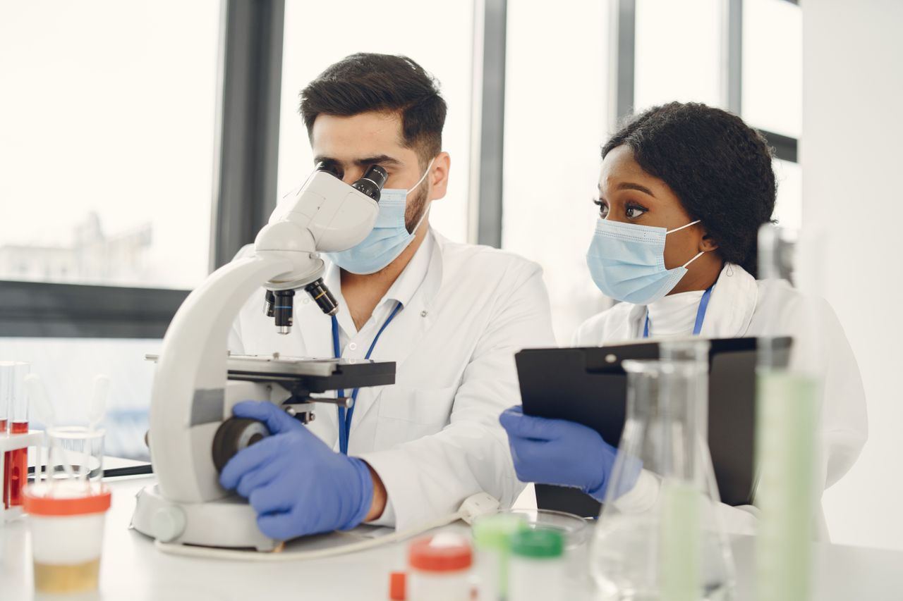 About Us Researchers using a microscope and taking notes in a modern lab.
